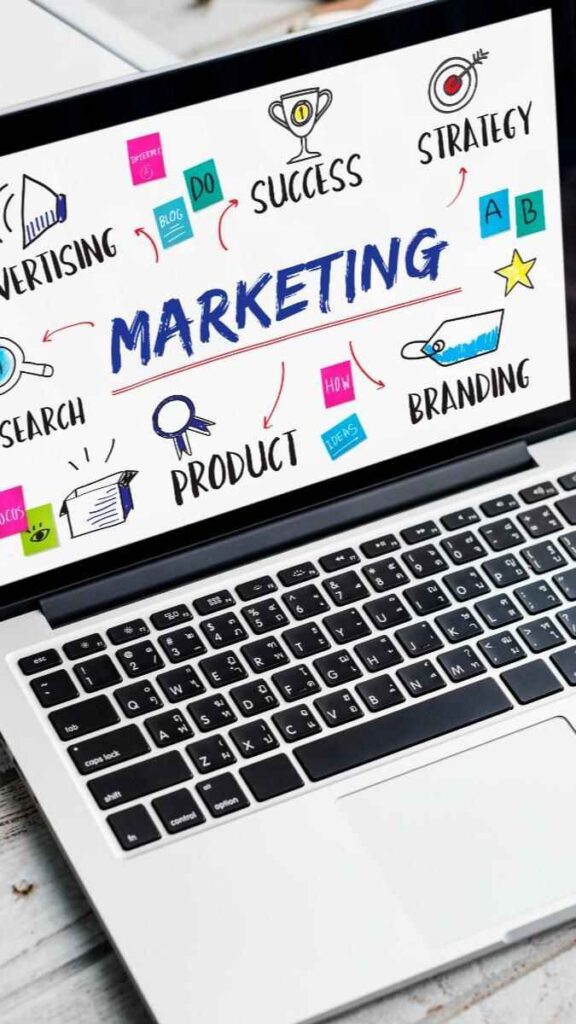 Digital Marketing Strategy Tips: A Complete Guide to Grow Your Business Online. A close-up, high-angle shot of an open laptop on a wooden surface. The screen displays a white background filled with colorful, hand-drawn-style digital marketing icons and keywords including "MARKETING," "STRATEGY," "SUCCESS," "PRODUCT," and "BRANDING." The laptop keyboard is visible in the foreground with a shallow depth of field.