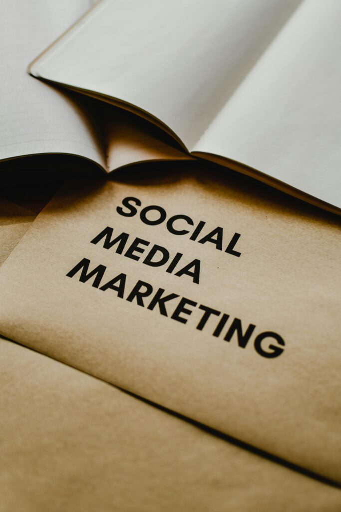 Social Media Marketing Tips: A Complete Guide to Grow Your Brand Online in 2026. A vertical, close-up shot of a tan or kraft paper sheet featuring the words "SOCIAL MEDIA MARKETING" printed in a clean, black sans-serif font. The paper is partially layered under the open white pages of a book or notebook in a soft, warm lighting environment.
